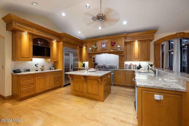 kitchen with sink, a breakfast bar, a kitchen island with sink, premium appliances, and light stone countertops