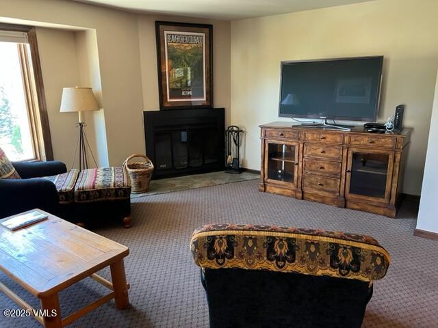 carpeted living area with a glass covered fireplace and baseboards