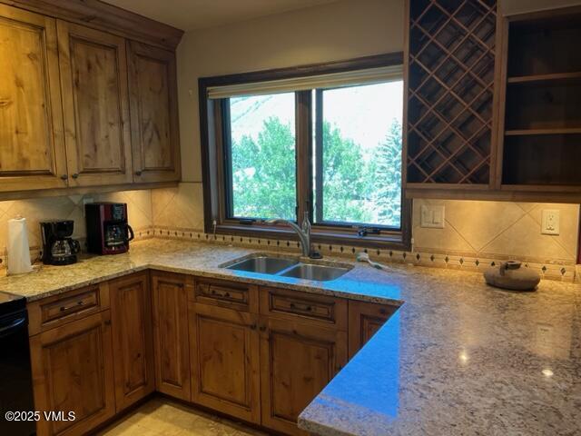 kitchen with tasteful backsplash, brown cabinetry, a sink, and light stone countertops