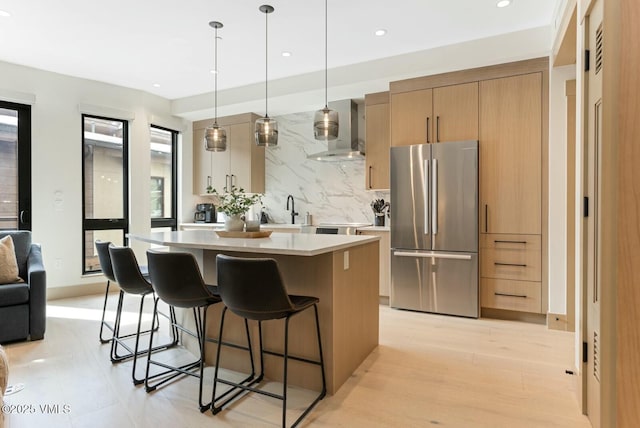 kitchen with a kitchen island, a kitchen breakfast bar, light countertops, freestanding refrigerator, and wall chimney exhaust hood