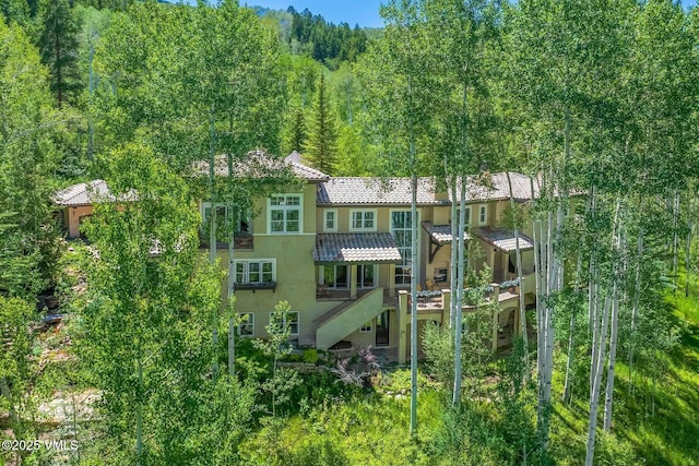 exterior space with stairs, a forest view, a tiled roof, and stucco siding