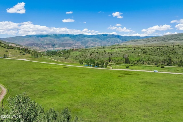 view of property's community featuring a rural view, a lawn, and a mountain view