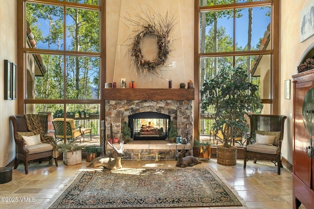 sitting room featuring a towering ceiling, baseboards, a stone fireplace, and stone tile floors