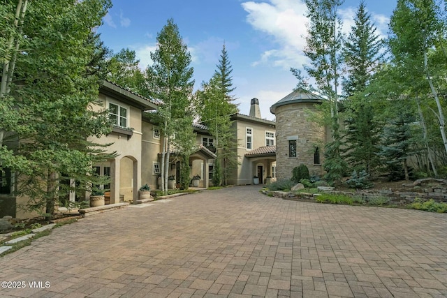 view of front of home featuring stone siding, decorative driveway, a chimney, and stucco siding