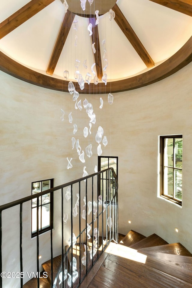 stairs with beamed ceiling, a towering ceiling, and wood finished floors