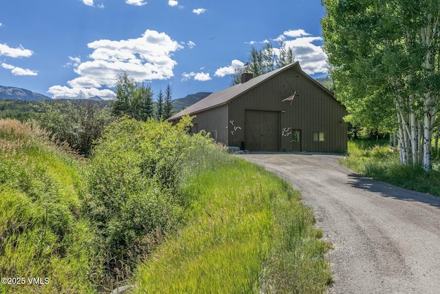 exterior space with driveway, a garage, a chimney, an outdoor structure, and a mountain view