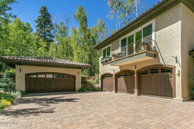 view of front of house with a balcony, a tile roof, decorative driveway, and stucco siding