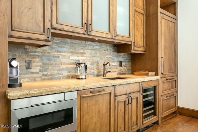 kitchen featuring stainless steel microwave, backsplash, glass insert cabinets, light stone countertops, and beverage cooler