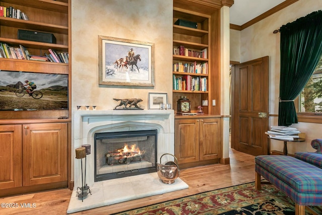 sitting room featuring light wood-type flooring, a warm lit fireplace, built in features, and ornamental molding