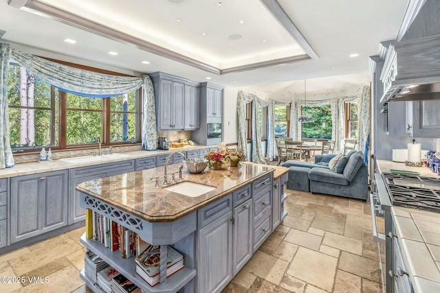 kitchen with stone tile flooring, gray cabinets, a raised ceiling, and a sink