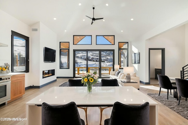 interior space with high vaulted ceiling, a glass covered fireplace, light wood-style flooring, and recessed lighting