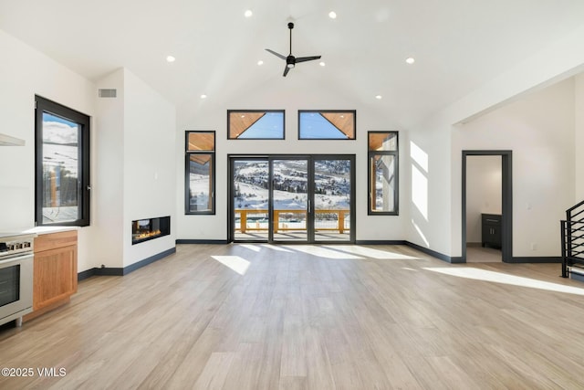 unfurnished living room with high vaulted ceiling, light wood finished floors, a glass covered fireplace, and baseboards