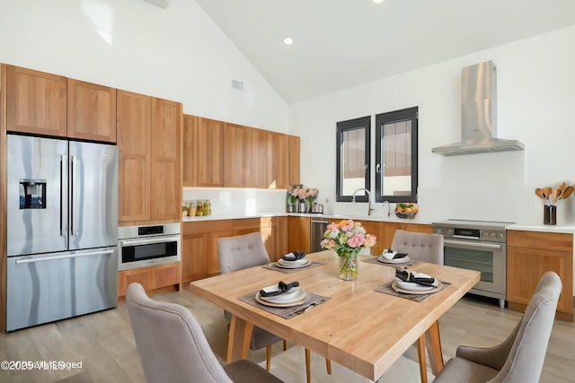 kitchen featuring stainless steel appliances, wall chimney range hood, light countertops, and visible vents