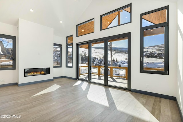 doorway with high vaulted ceiling, a glass covered fireplace, baseboards, and wood finished floors