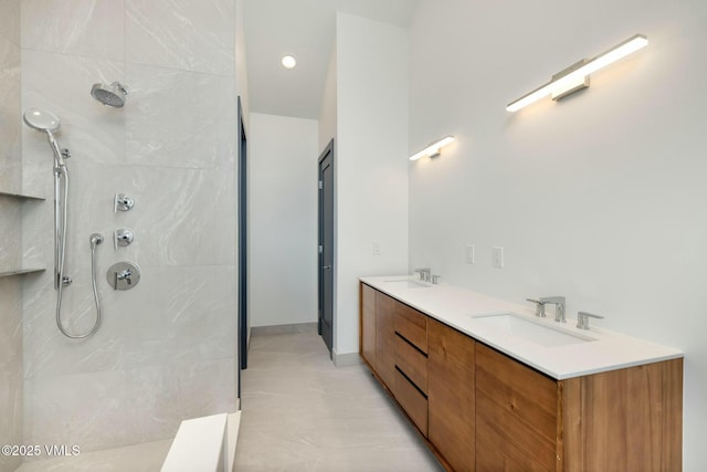 bathroom featuring a tile shower, double vanity, and a sink