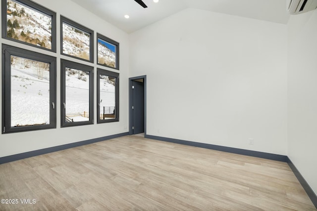 empty room featuring light wood finished floors, baseboards, a wall unit AC, ceiling fan, and high vaulted ceiling