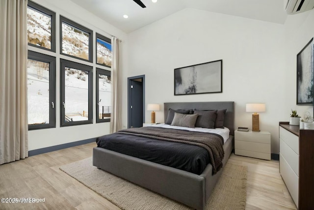 bedroom featuring light wood-style floors, baseboards, high vaulted ceiling, and a wall mounted air conditioner