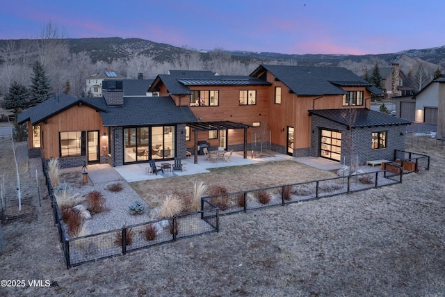 back of property at dusk featuring a standing seam roof, fence, a mountain view, a chimney, and a patio area