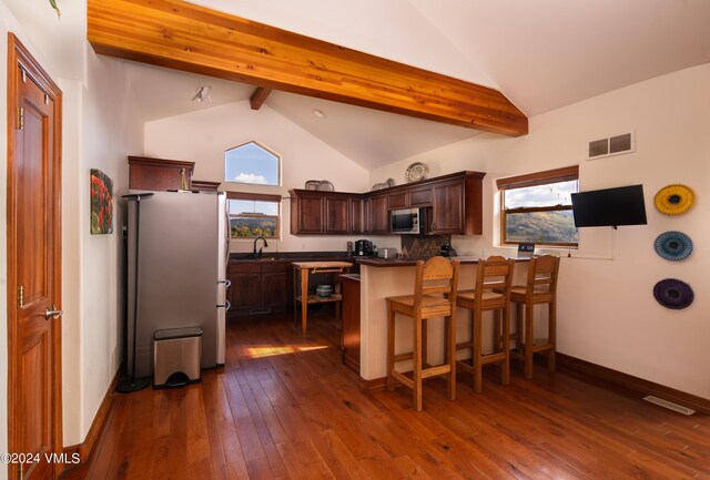 kitchen with a breakfast bar, appliances with stainless steel finishes, dark hardwood / wood-style floors, kitchen peninsula, and beam ceiling