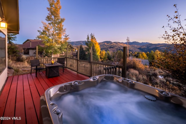 deck at dusk featuring an outdoor hot tub, a mountain view, and a fire pit