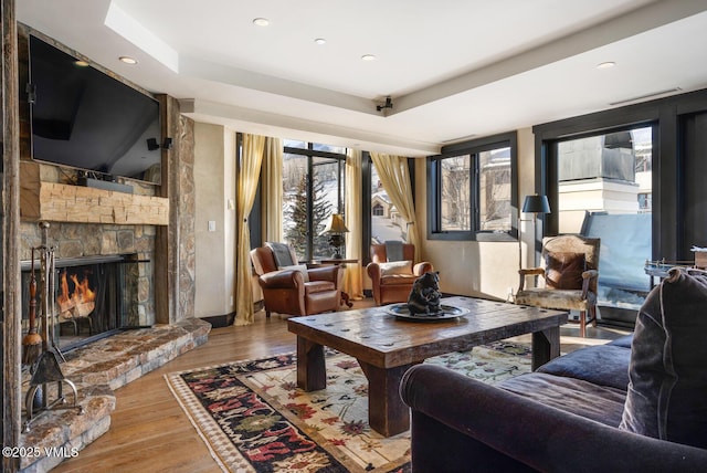 living area with a fireplace, a tray ceiling, wood finished floors, and recessed lighting