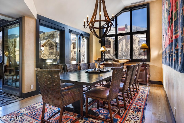 dining space with baseboards, high vaulted ceiling, hardwood / wood-style flooring, and an inviting chandelier