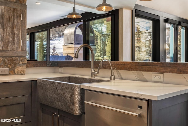 kitchen with light stone counters, hanging light fixtures, a sink, dark brown cabinets, and dishwasher