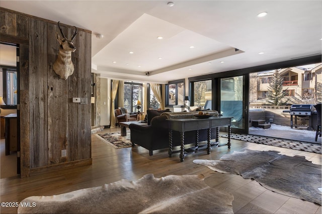 living room featuring recessed lighting, a raised ceiling, wooden walls, and wood finished floors