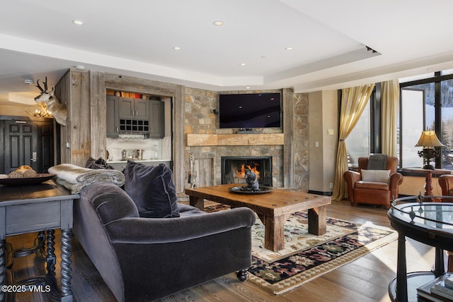 living area with a fireplace, a raised ceiling, wood finished floors, and recessed lighting