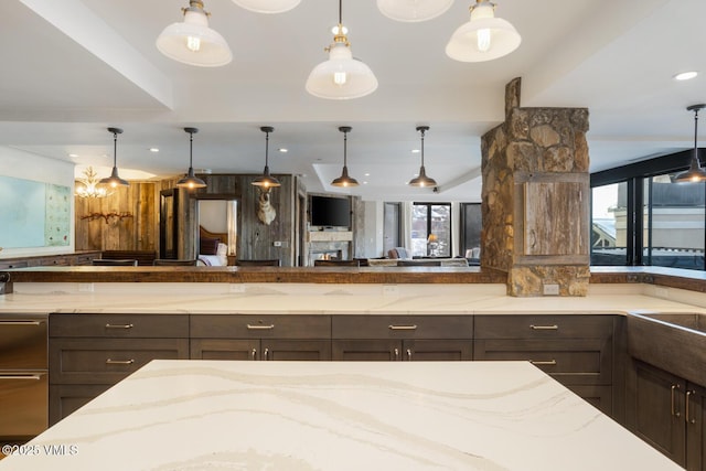 kitchen featuring open floor plan, decorative light fixtures, dark brown cabinets, and light stone countertops