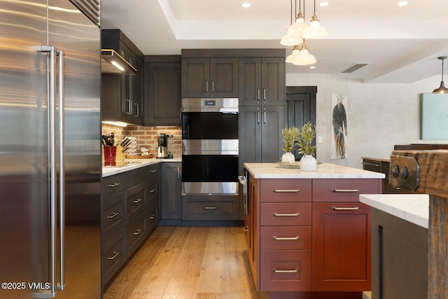 kitchen with decorative backsplash, stainless steel appliances, light countertops, light wood-type flooring, and pendant lighting