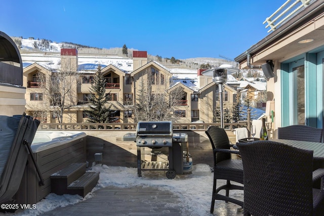 snow covered patio featuring a mountain view, a hot tub, a balcony, and grilling area