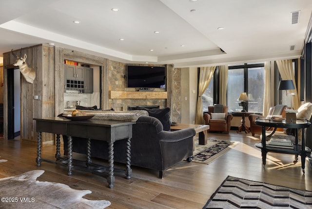 living area with a large fireplace, visible vents, a tray ceiling, and hardwood / wood-style floors