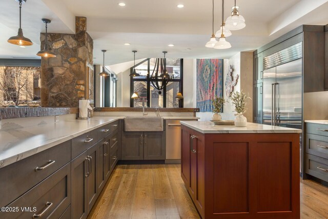 kitchen featuring appliances with stainless steel finishes, pendant lighting, light wood-style floors, and a sink