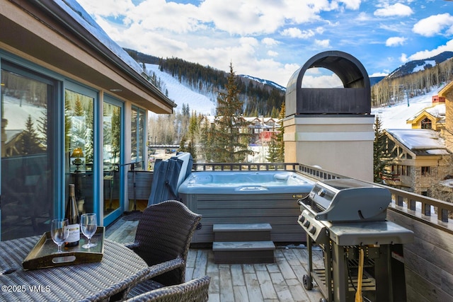 snow covered deck featuring a grill, a mountain view, and a hot tub