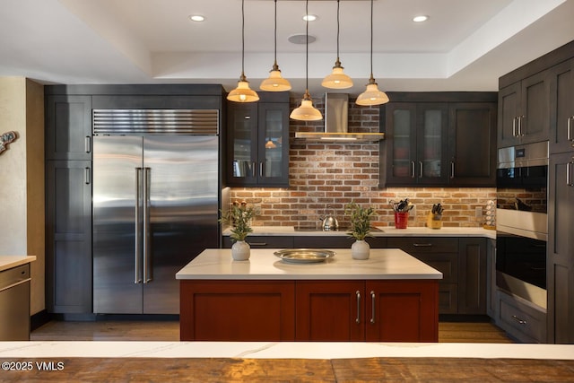 kitchen featuring wall chimney exhaust hood, pendant lighting, stainless steel appliances, and light countertops