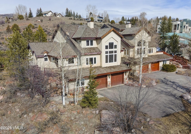 view of front of house featuring aphalt driveway, an attached garage, a chimney, and stucco siding