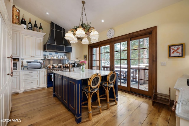 kitchen featuring premium range hood, french doors, a center island with sink, light stone countertops, and white cabinets