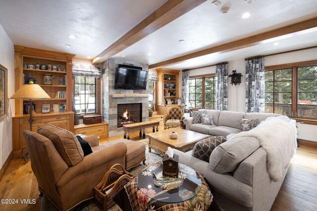 living room with built in features, a fireplace, beam ceiling, and light hardwood / wood-style flooring