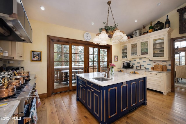 kitchen featuring sink, blue cabinetry, high end stainless steel range oven, ventilation hood, and a center island with sink