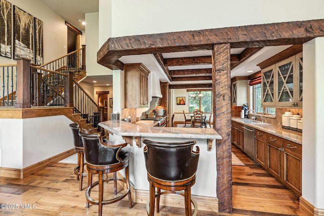 825 Forest Rd Unit 2, Vail, CO 81657 - kitchen featuring light wood-type flooring, stainless steel dishwasher, a breakfast bar, glass insert cabinets, and beam ceiling