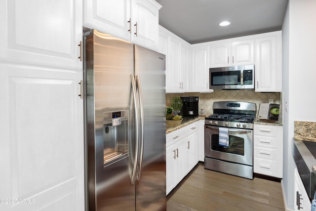 kitchen with wood finished floors, light stone countertops, stainless steel appliances, white cabinetry, and backsplash