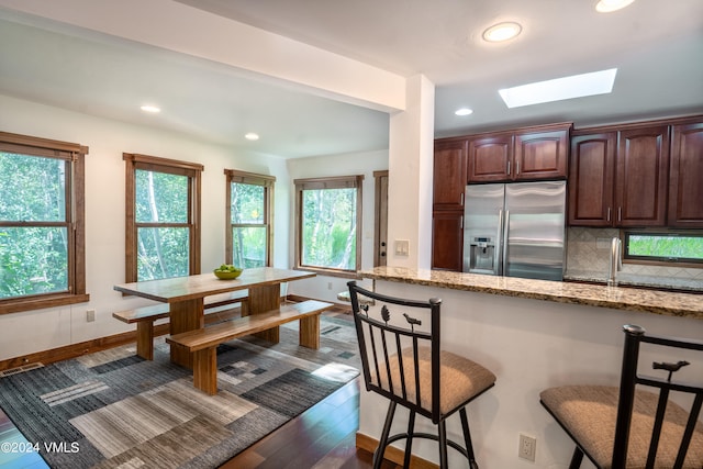 kitchen with light stone counters, a skylight, backsplash, stainless steel fridge, and a kitchen bar