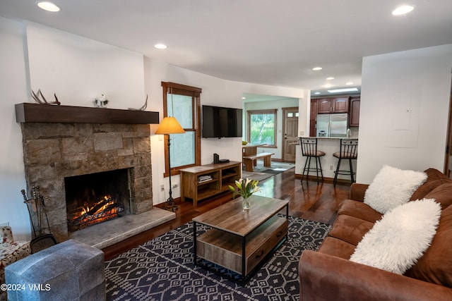 living area featuring recessed lighting, baseboards, dark wood-type flooring, and a stone fireplace