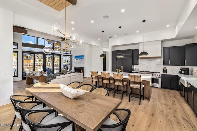 dining room with baseboards, a high ceiling, recessed lighting, a warm lit fireplace, and light wood-type flooring