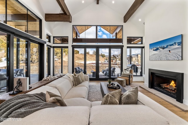 living room with beam ceiling, wood finished floors, a warm lit fireplace, and high vaulted ceiling