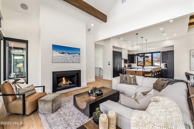 living room featuring a lit fireplace, beam ceiling, recessed lighting, light wood-style floors, and high vaulted ceiling