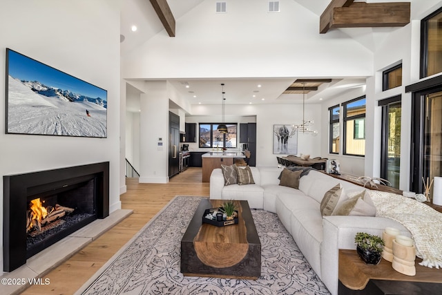 living room with visible vents, light wood-type flooring, a lit fireplace, beam ceiling, and high vaulted ceiling