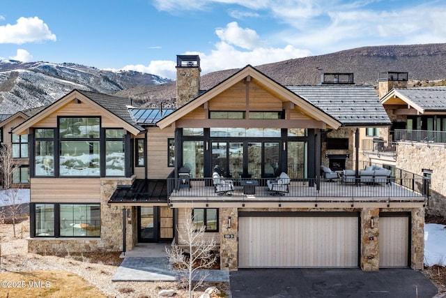 view of front facade featuring a standing seam roof, an attached garage, a chimney, aphalt driveway, and a mountain view