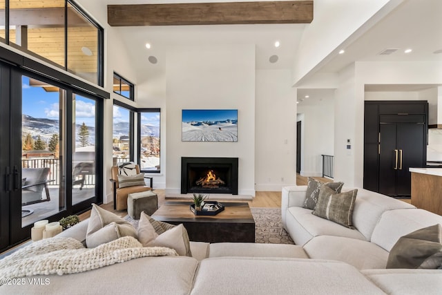 living room with beamed ceiling, visible vents, light wood-type flooring, and a lit fireplace